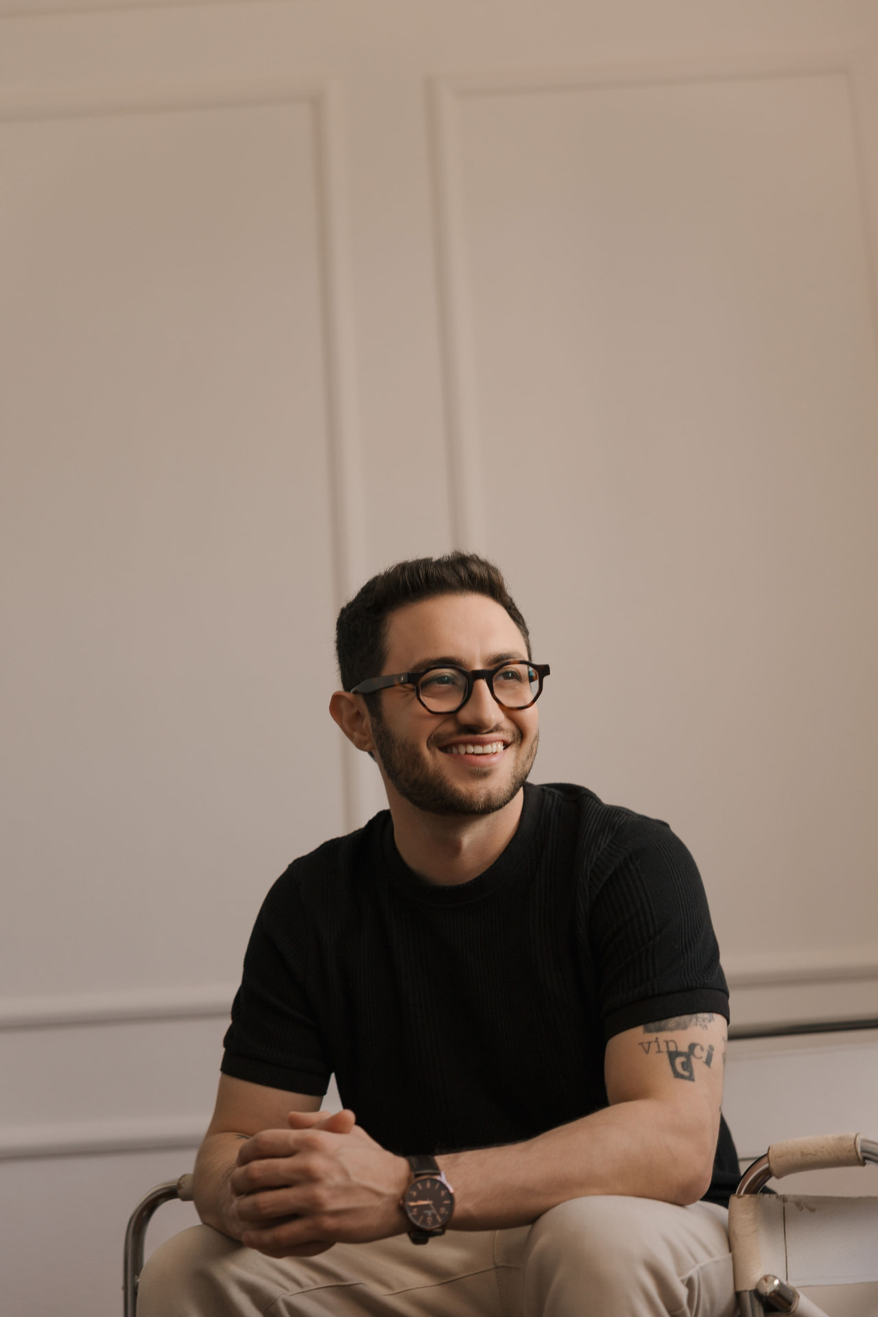Lucas Vincci sorrindo, de camiseta preta e óculos, olhando para o lado